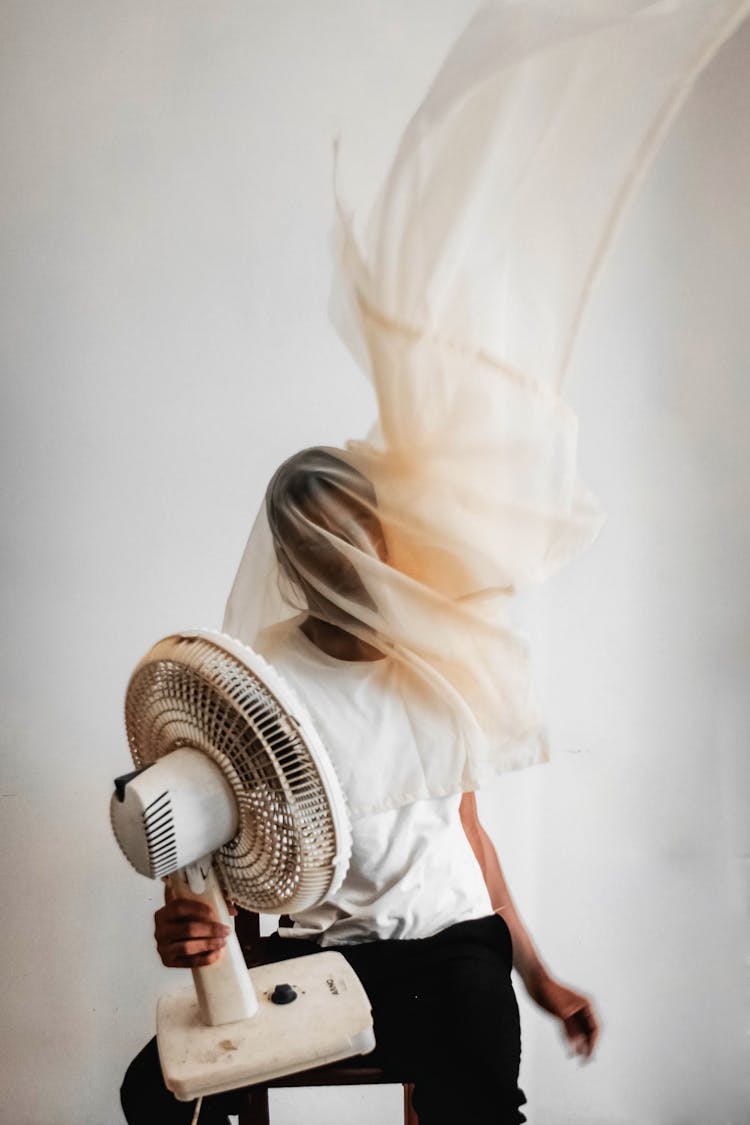 Man Wearing White Crew-neck T-shirt While Holding White Desk Fan