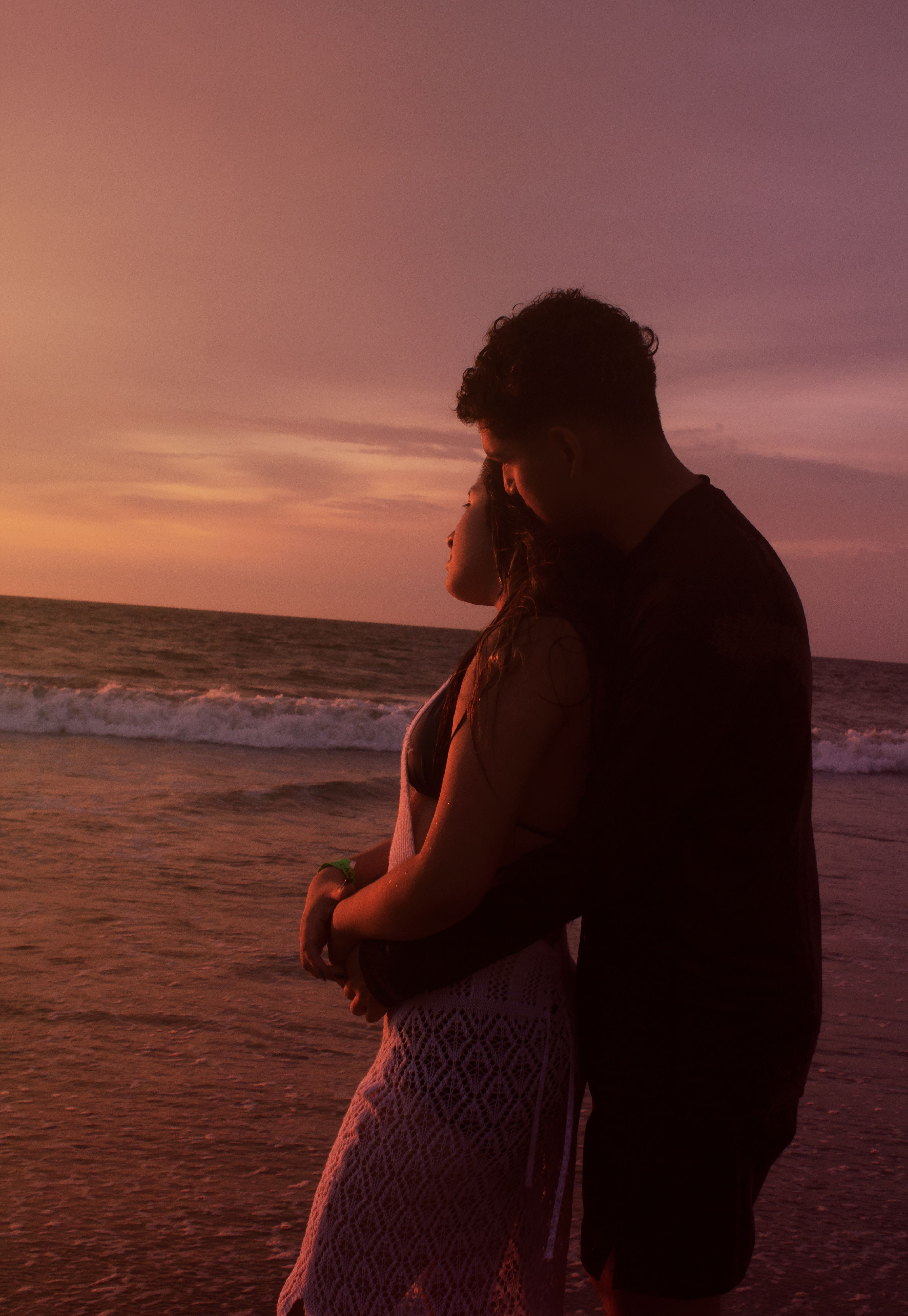 Gratis Una coppia si abbraccia su una spiaggia al tramonto, immortalando amore e romanticismo in riva al mare. Foto a disposizione