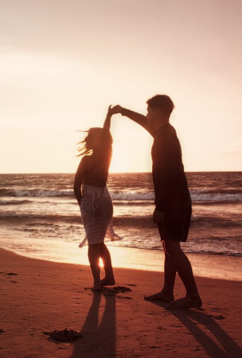 Free A couple gracefully dancing on the beach at sunset, casting silhouettes against the ocean. Stock Photo