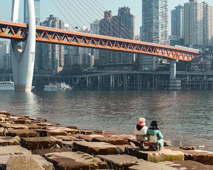 People enjoying a scenic view by the waterfront with a modern bridge and skyscrapers in the backdrop.