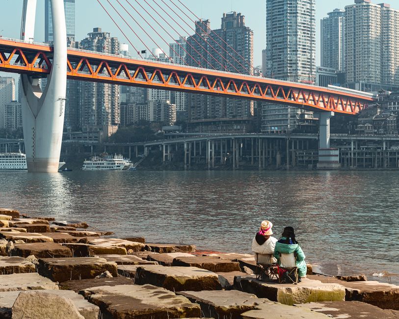 People enjoying a scenic view by the waterfront with a modern bridge and skyscrapers in the backdrop.