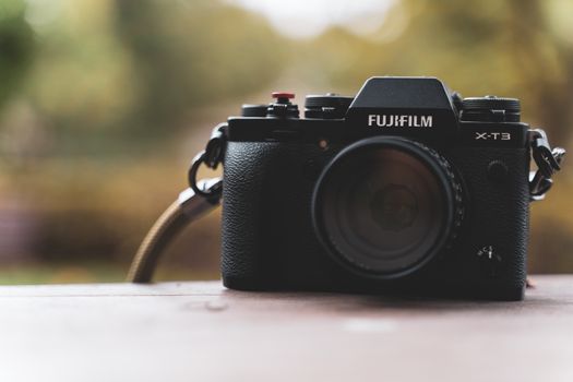 Fujifilm X-T3 camera placed on a wooden table, set against a blurred autumn background.