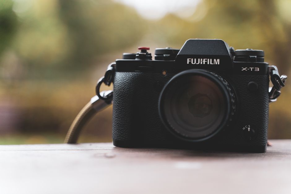 Fujifilm X-T3 camera placed on a wooden table, set against a blurred autumn background.
