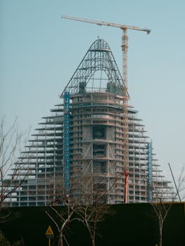 Skyscraper under construction with crane against clear sky.