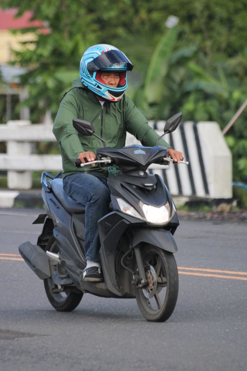 Free Adult male riding a scooter in casual attire and helmet on a city street. Stock Photo