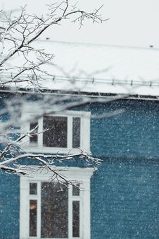 A blue house in Tromsø, Norway, covered in snow with falling flakes, conveying a serene winter atmosphere.