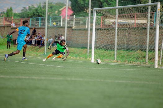 Intense soccer match action with goalkeeper diving to save a goal against a forward's strike.