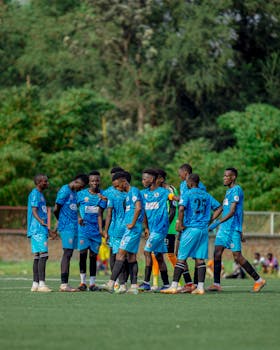 A soccer team in blue jerseys huddling before a match on a sunny day outdoors.