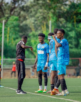 Coach instructing soccer players during daytime practice on green field.