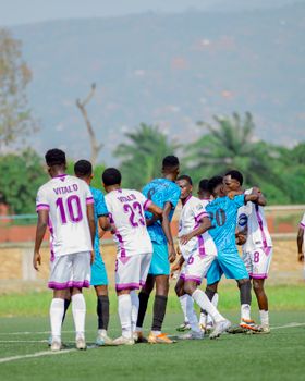 Players from two soccer teams greeting each other on the field during a sunny match day.