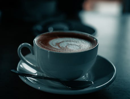 A serene close-up of a cappuccino cup with a spoon on a saucer in a moody setting.