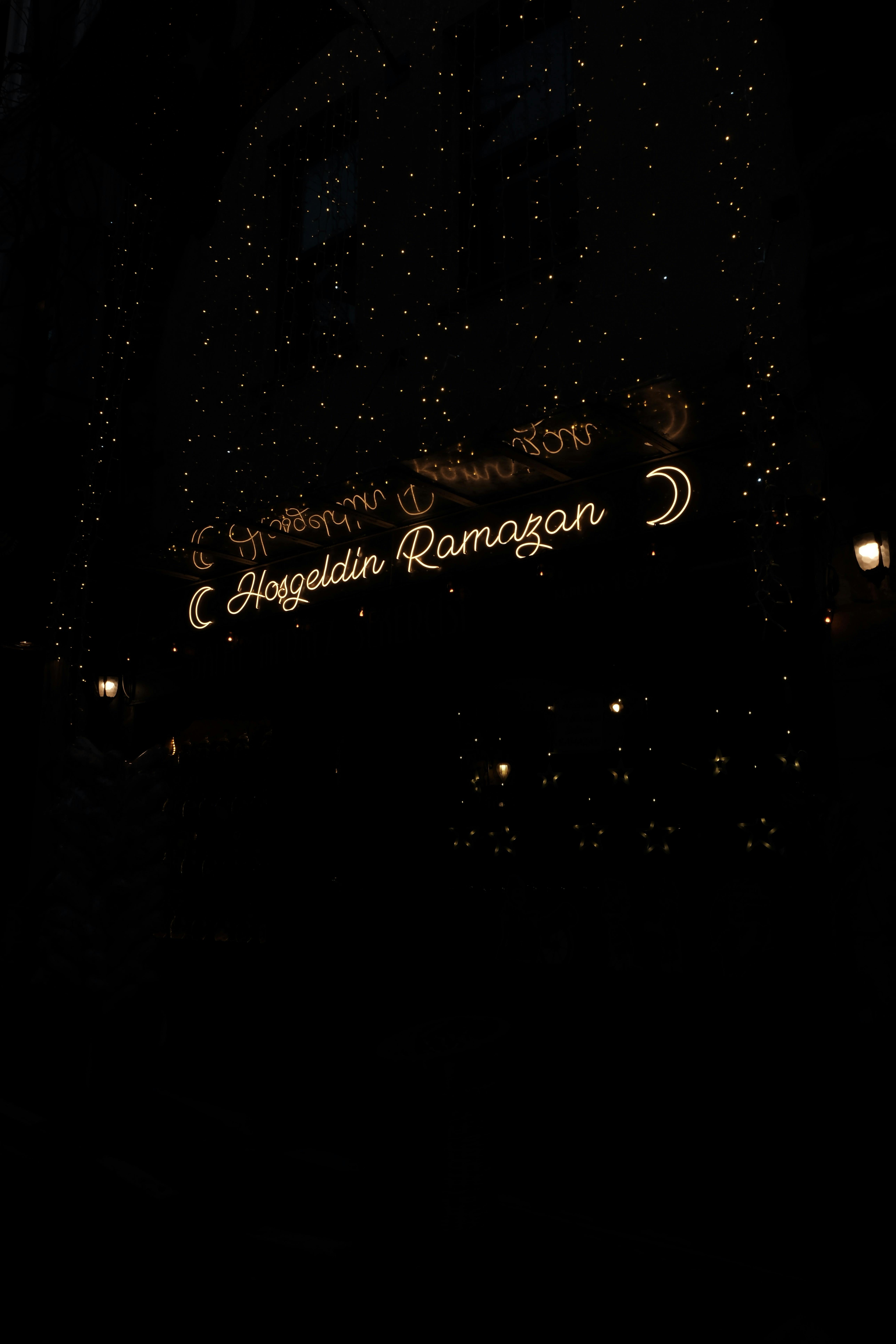 Glowing 'Hoşgeldin Ramazan' sign with crescent moon lights at night, festive atmosphere.