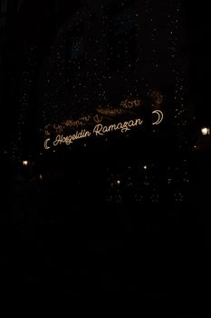 Glowing 'Hoşgeldin Ramazan' sign with crescent moon lights at night, festive atmosphere.