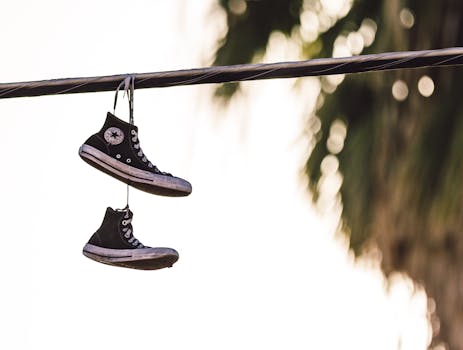Two worn sneakers hanging on a powerline against a blurred background, evoking urban nostalgia.