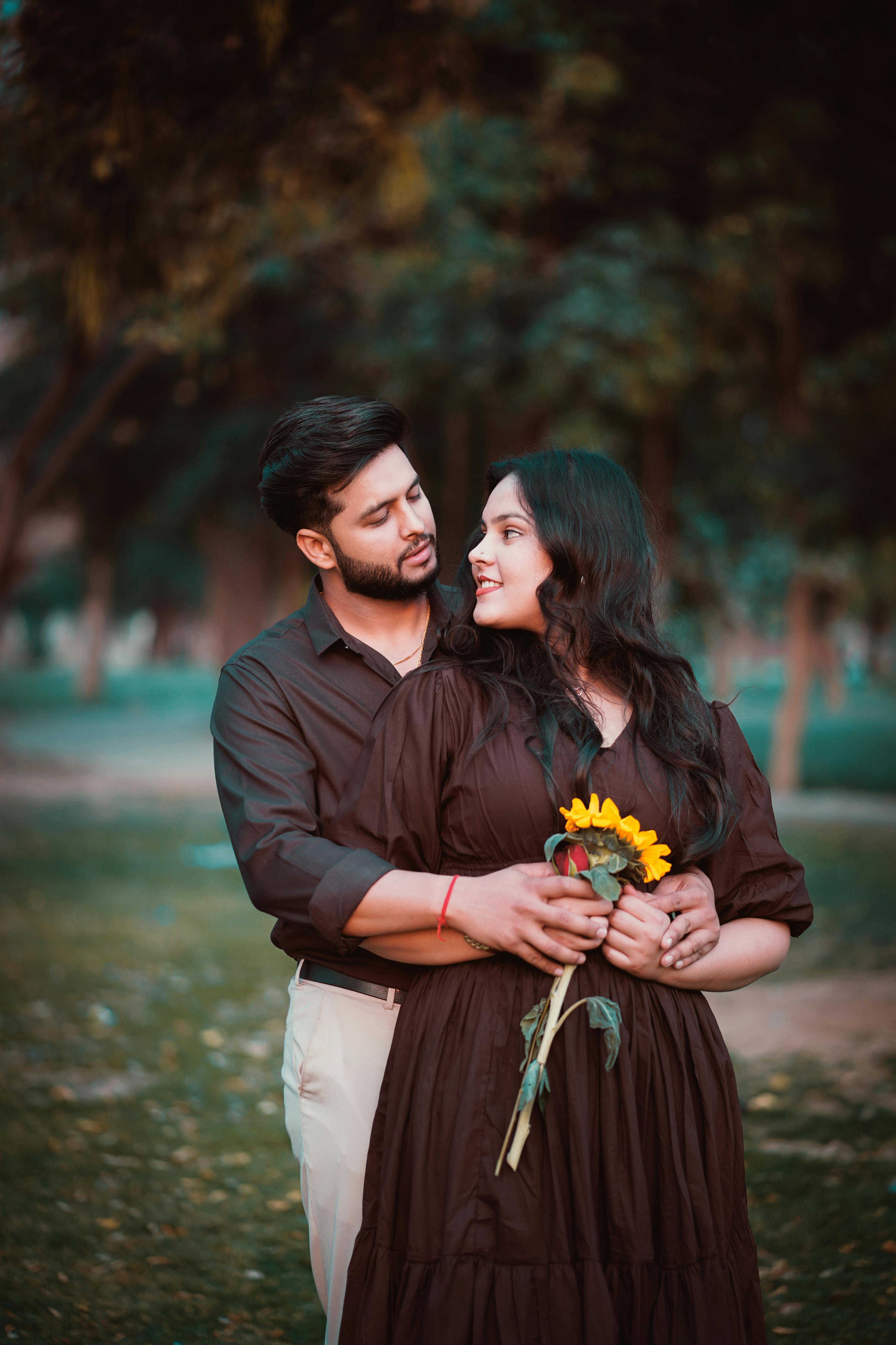 A couple enjoying an intimate outdoor photoshoot, holding a sunflower in a serene park.