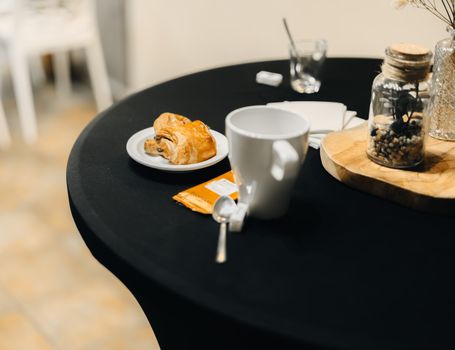 A cozy coffee setup featuring a croissant, mug, and decorative jar on a round table. Perfect for a relaxing brunch.