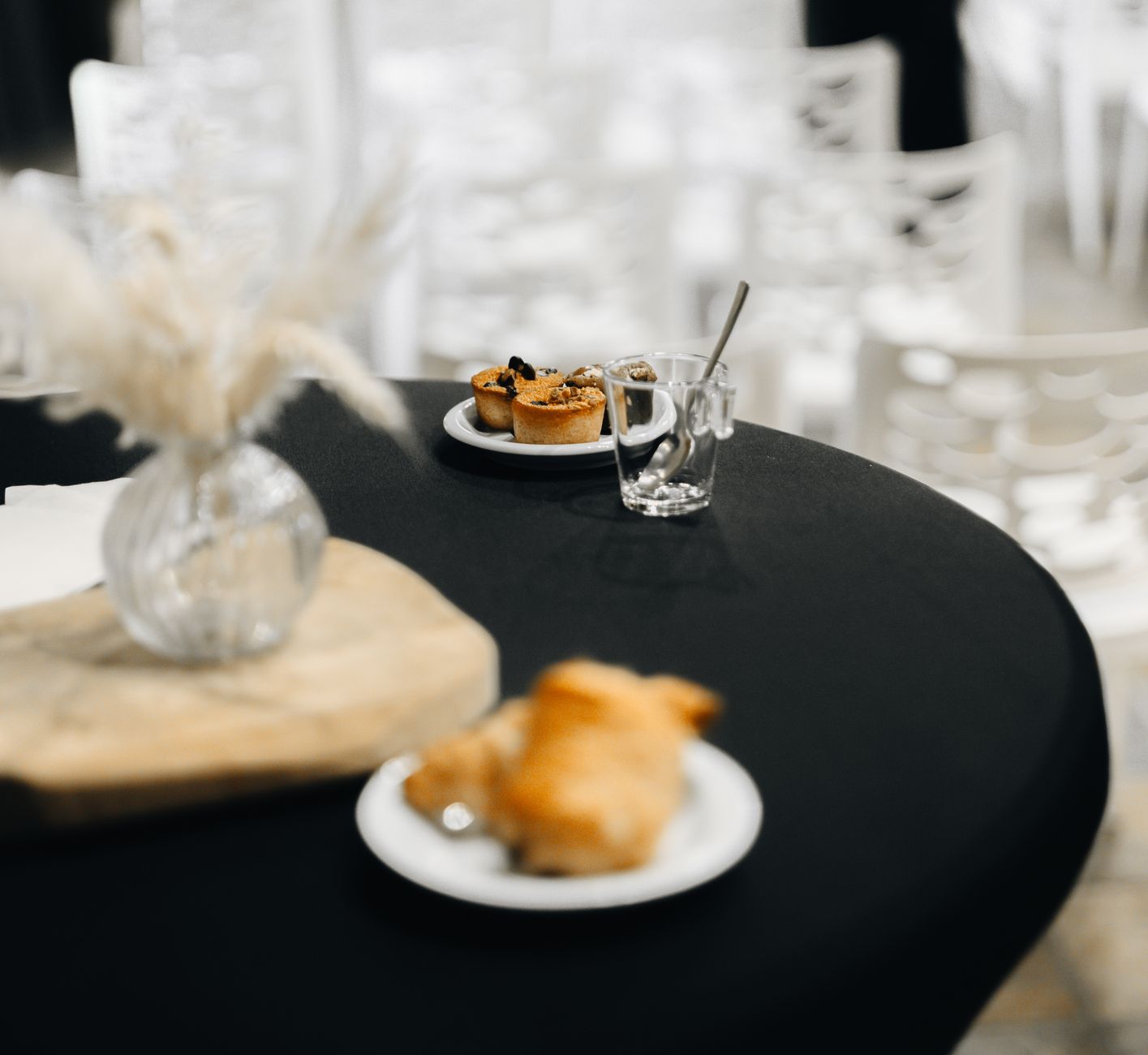 Elegant table setting with pastries, a glass vase, and a blurred background at an indoor event.