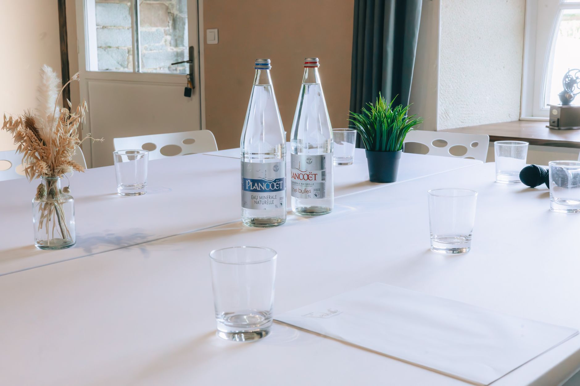 Clean conference room table with water bottles, glasses, and decorative plants, ready for meeting.