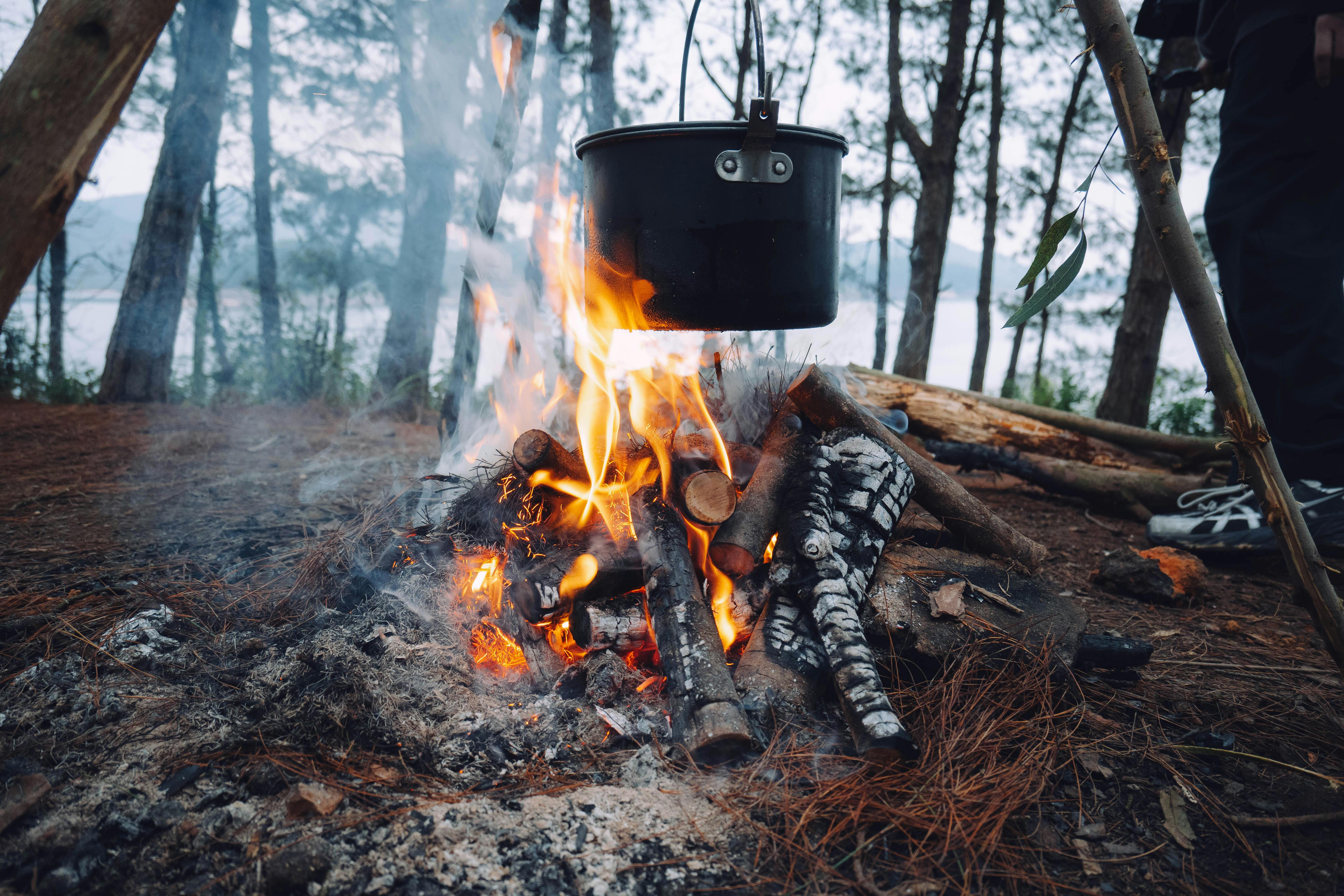 A pot hanging over a campfire in a serene forest, perfect for outdoor adventure enthusiasts.