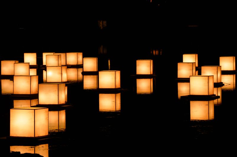 Floating lanterns glowing warm on dark water at night — photo by Guo Lang on Pexels