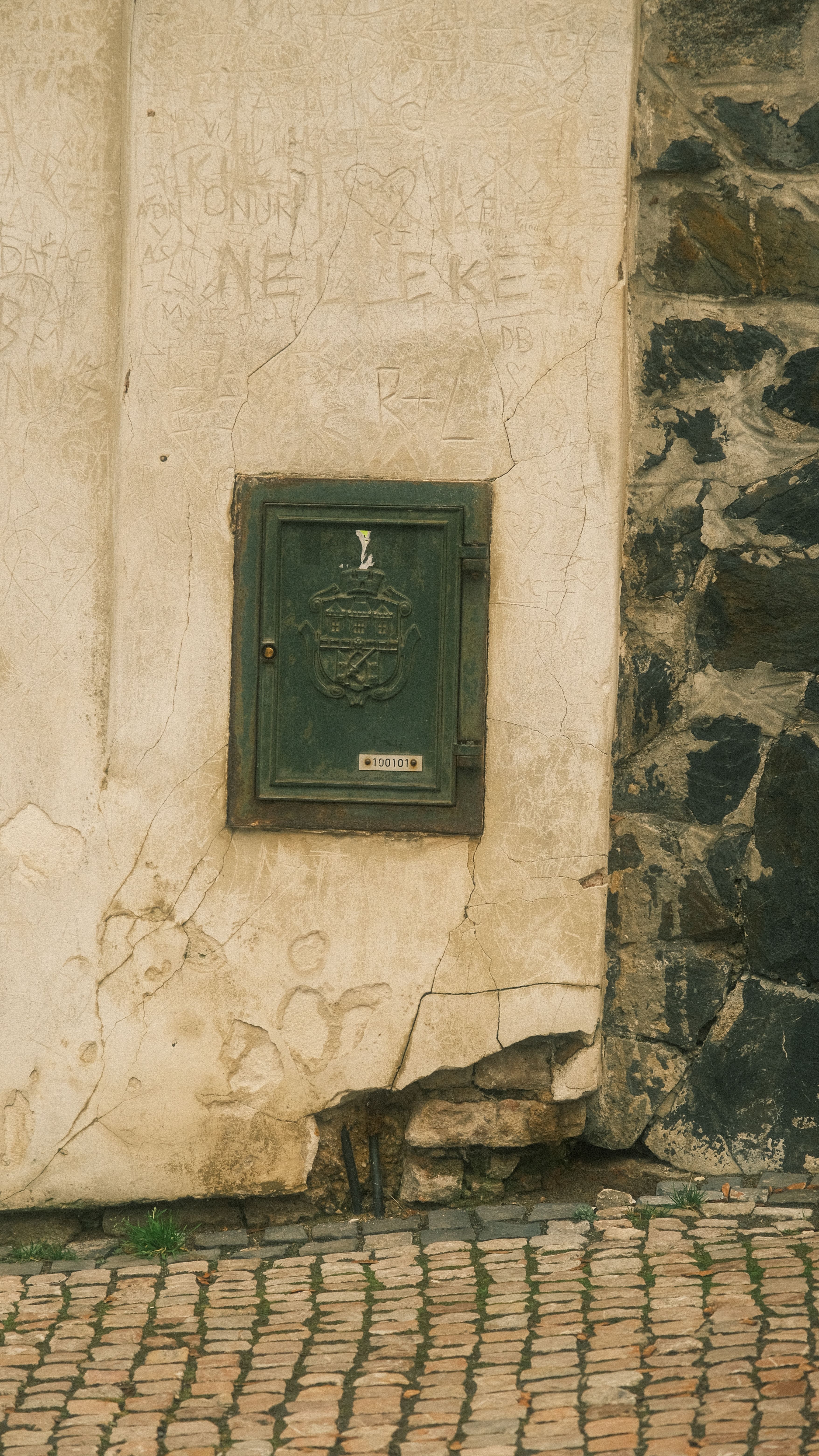 A weathered wall with a green metal door and cobblestone path, showcasing vintage urban texture.