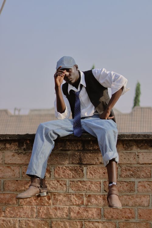 Free Fashionable young man in casual outfit sitting confidently on a brick wall outdoors. Stock Photo