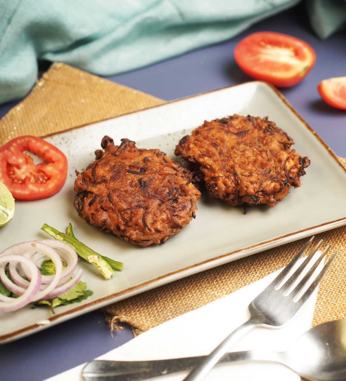 Golden vegetable fritters garnished with fresh tomatoes and onions on a ceramic plate