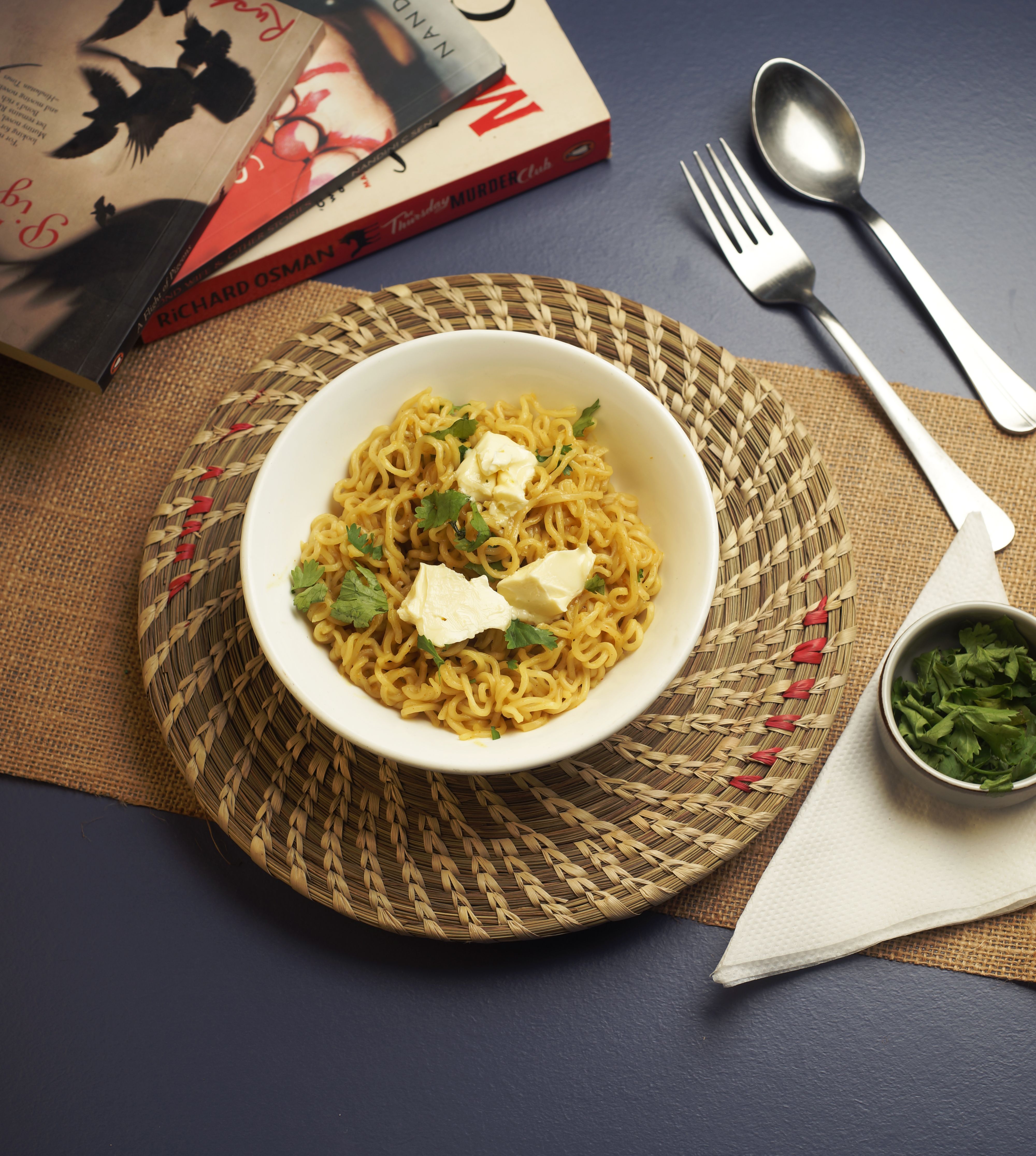 Spicy noodles garnished with herbs and cheese, with books and cutlery.