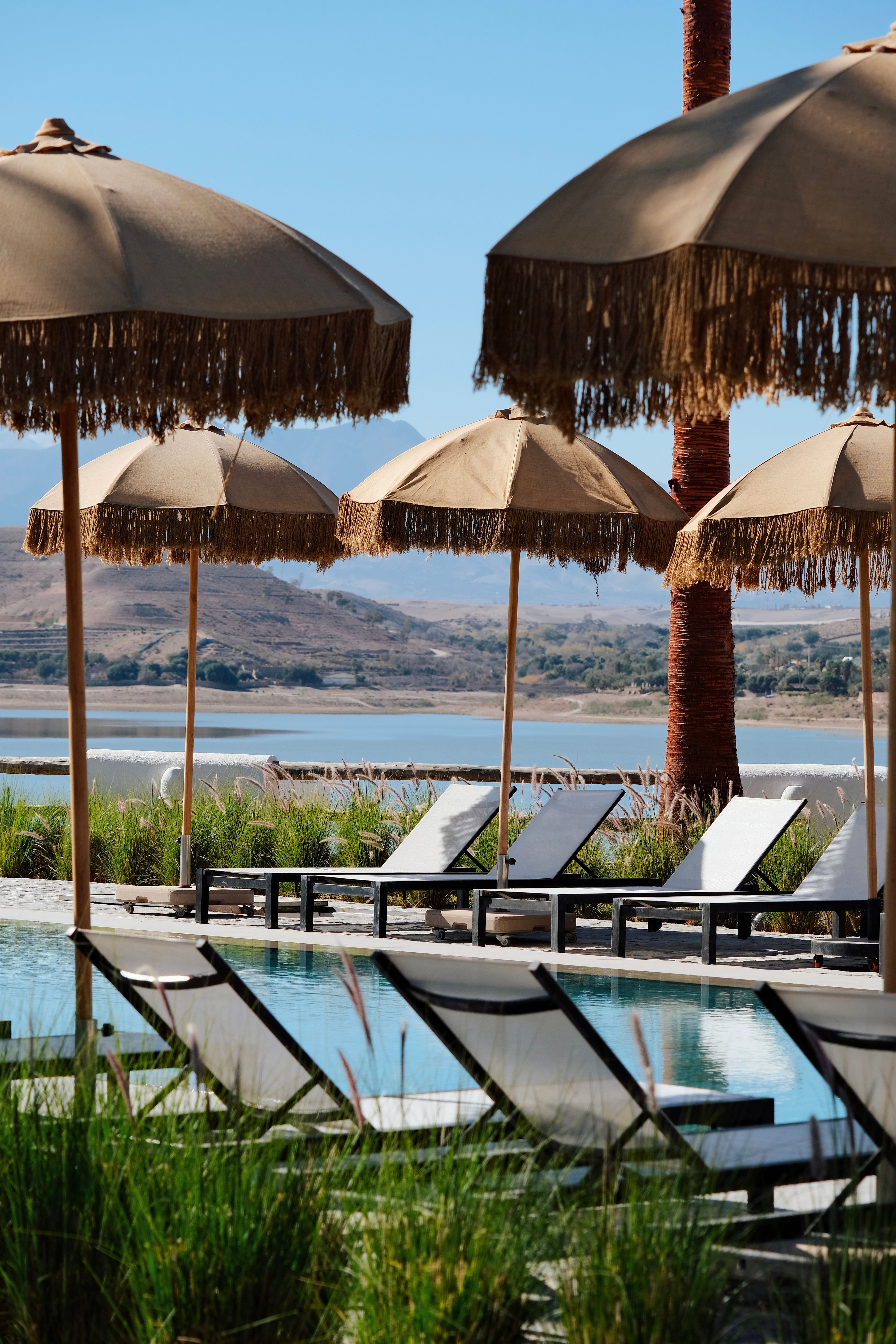 Serene poolside scene with sunbeds and parasols overlooking a peaceful lake in Aguergour, Morocco.