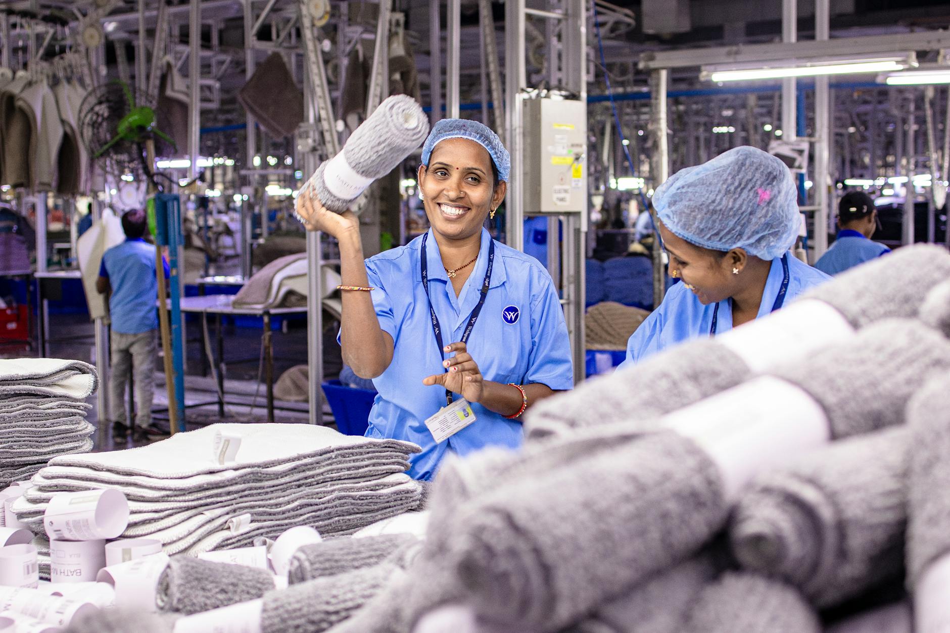 Smiling textile workers in an Indian factory organize fabric rolls, showcasing teamwork.