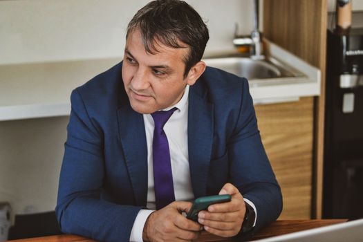 Professionele man in kantooromgeving met smartphone, gekleed in een blauw pak. Ideaal voor zakelijke of bedrijfsthema's.