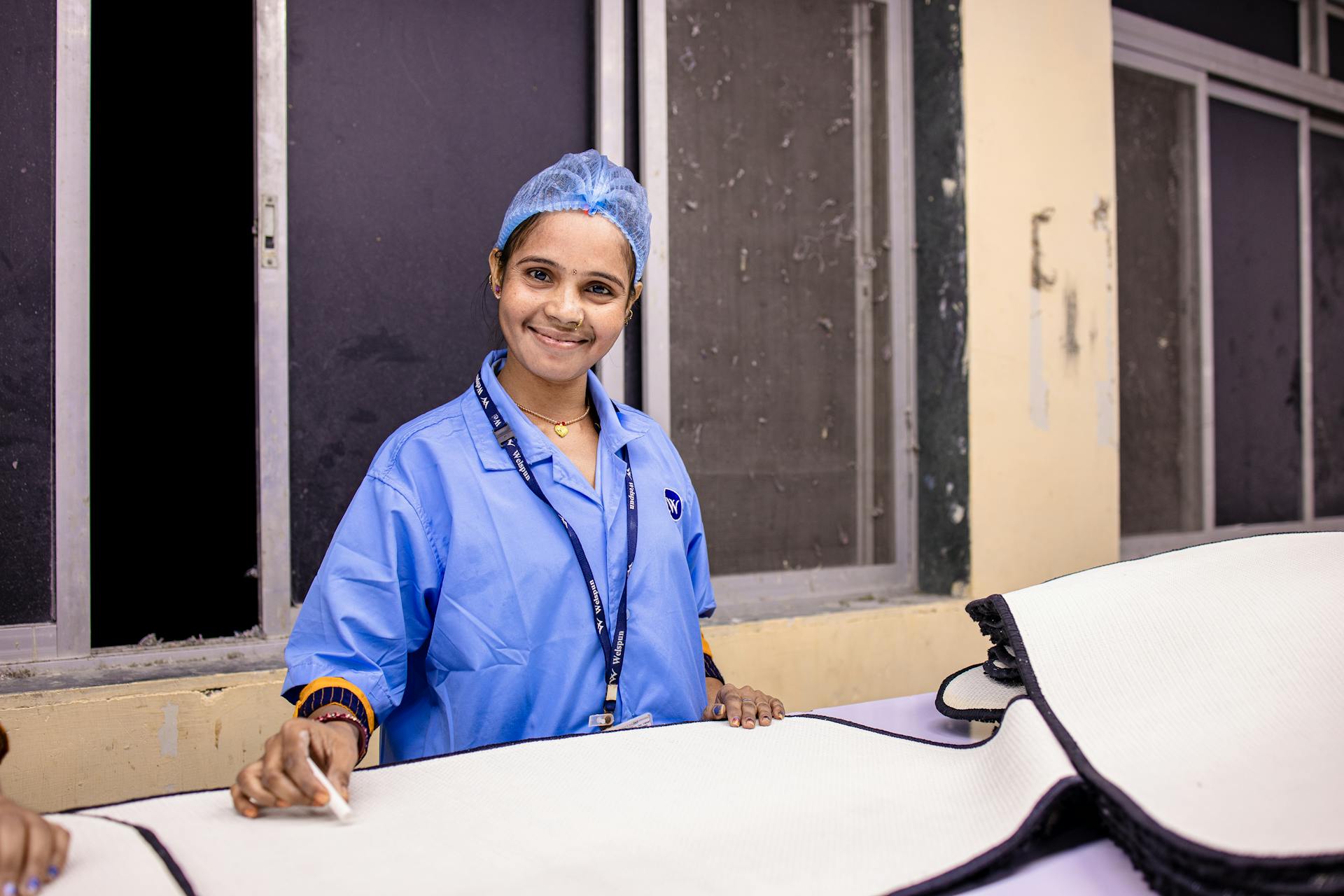 Portrait of a woman in a blue uniform smiling at her work station indoors.