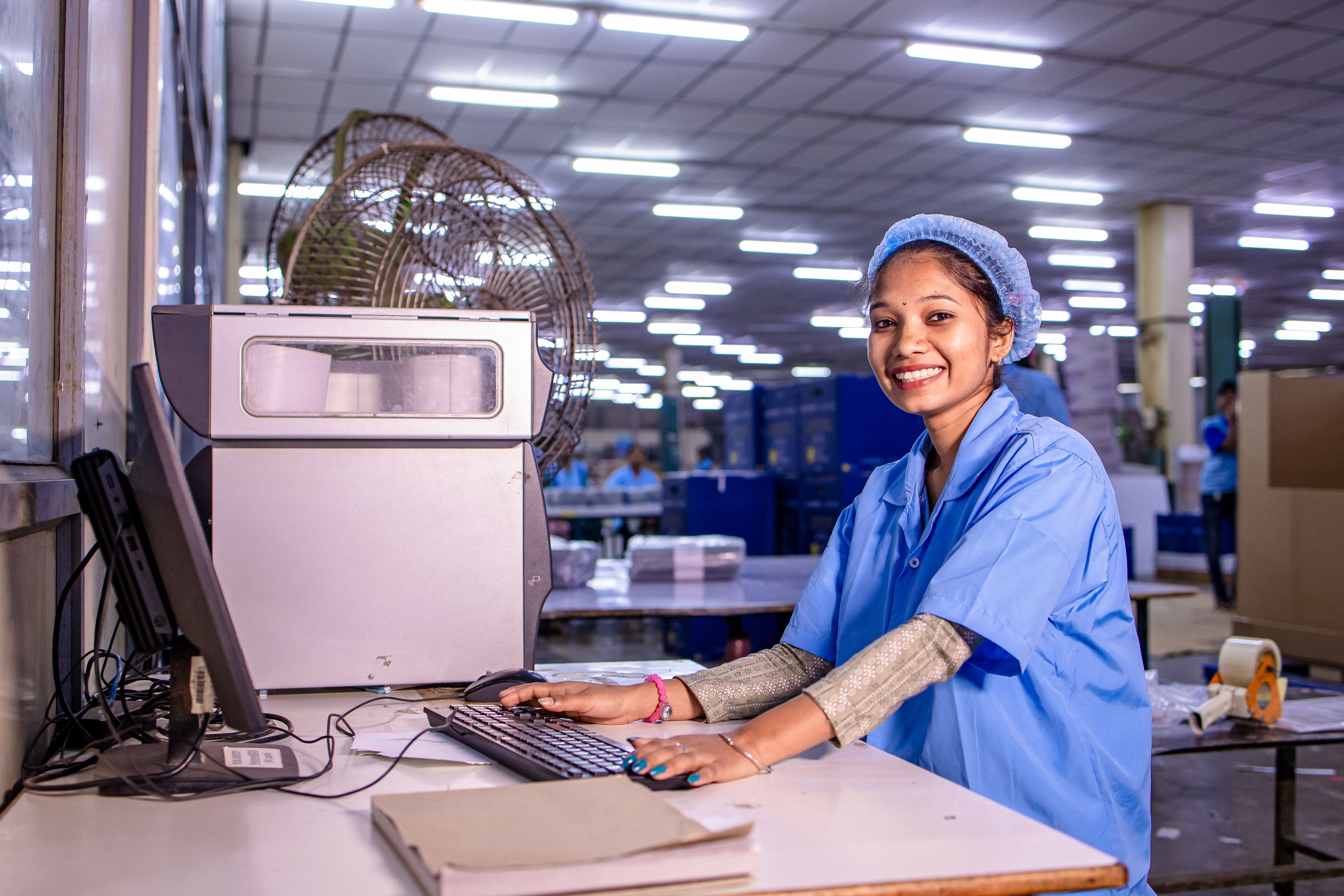 Portrait of a smiling female factory worker at her desk in a brightly lit production facility.