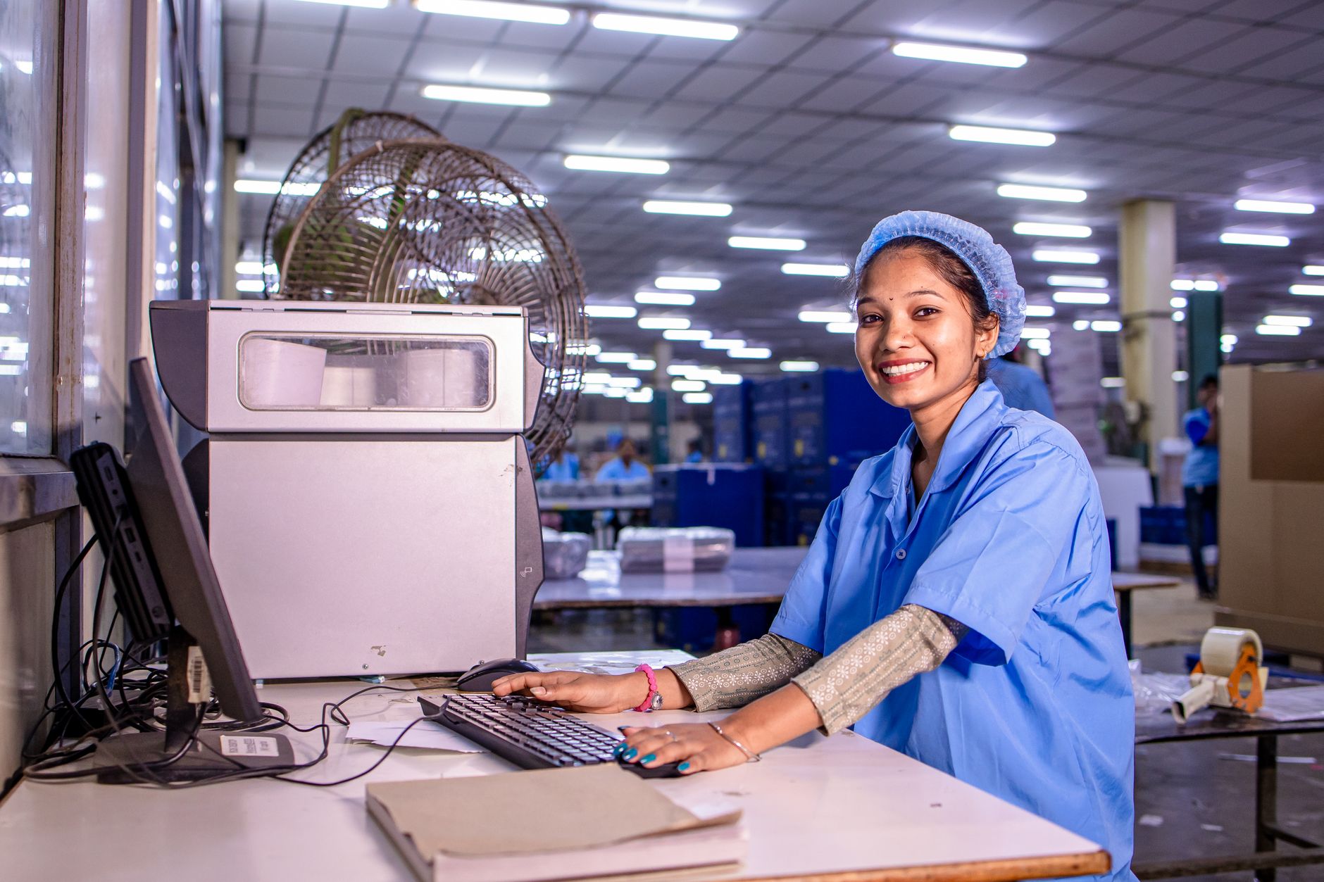 Portrait of a smiling female factory worker at her desk in a brightly lit production facility.