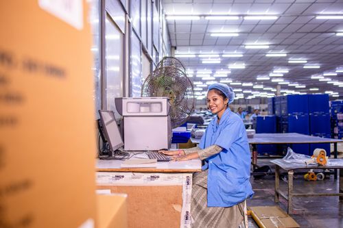 Free A cheerful female worker at a computer station in a busy warehouse environment. Stock Photo