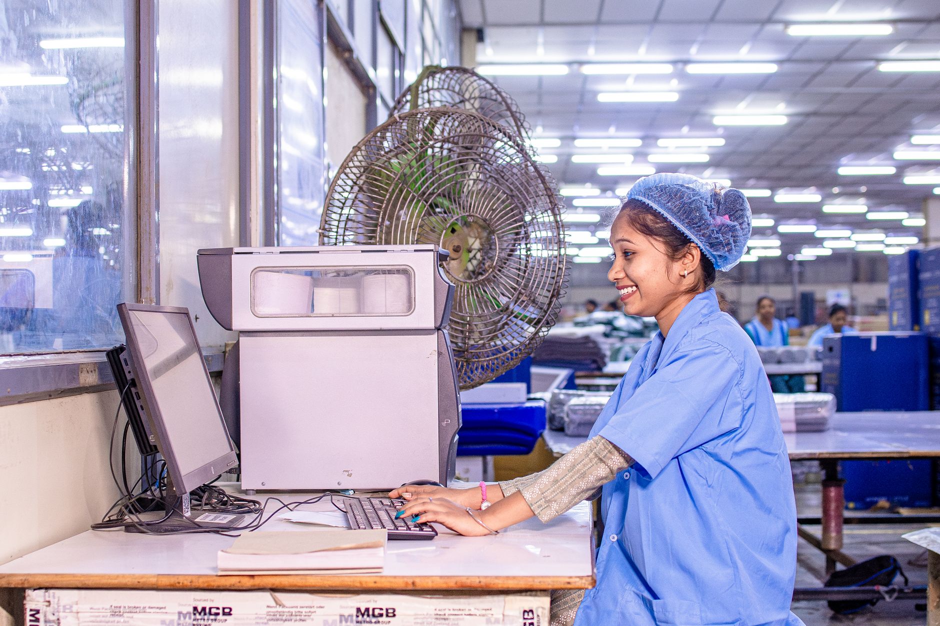 Smiling female worker using computer in a well-lit factory environment.
