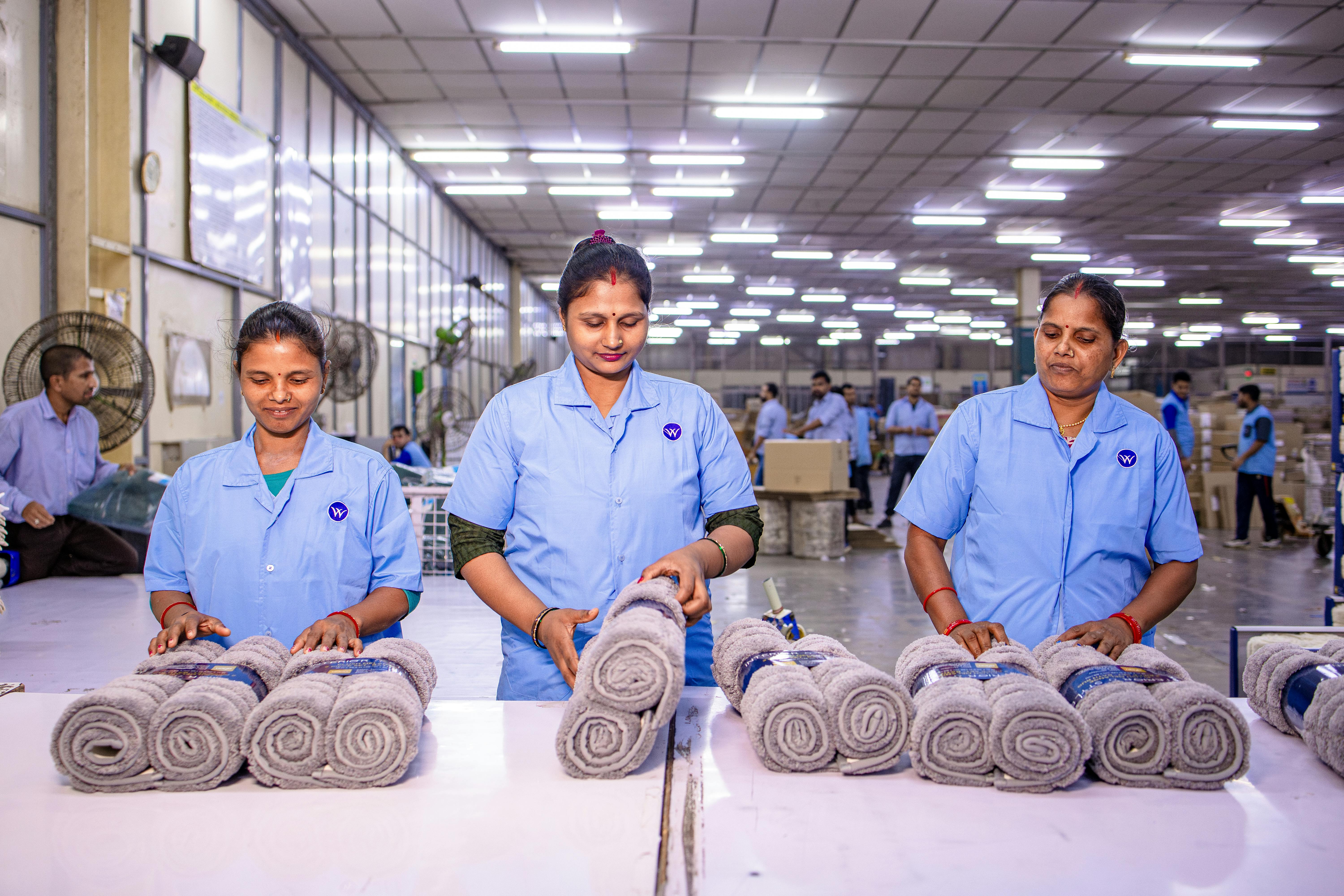 Three female workers inspecting rolled towels at a textile factory, showcasing teamwork and quality control.
