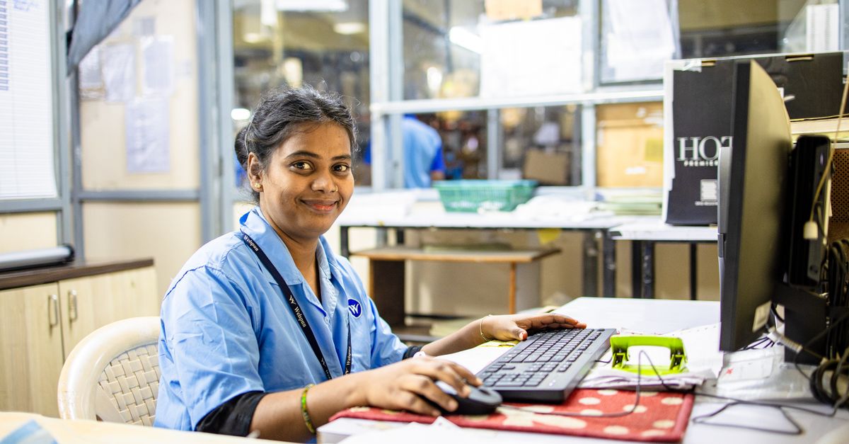Young professional smiling at her desk in a modern office setting, engaging in computer work.