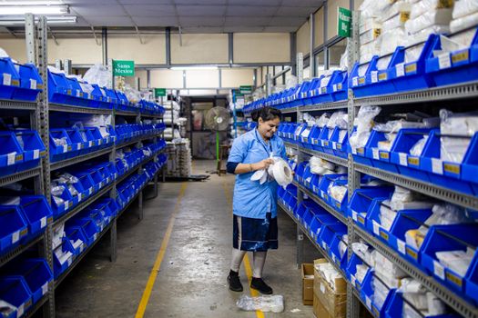 A woman organizing inventory in a warehouse aisle, surrounded by shelves and blue bins.