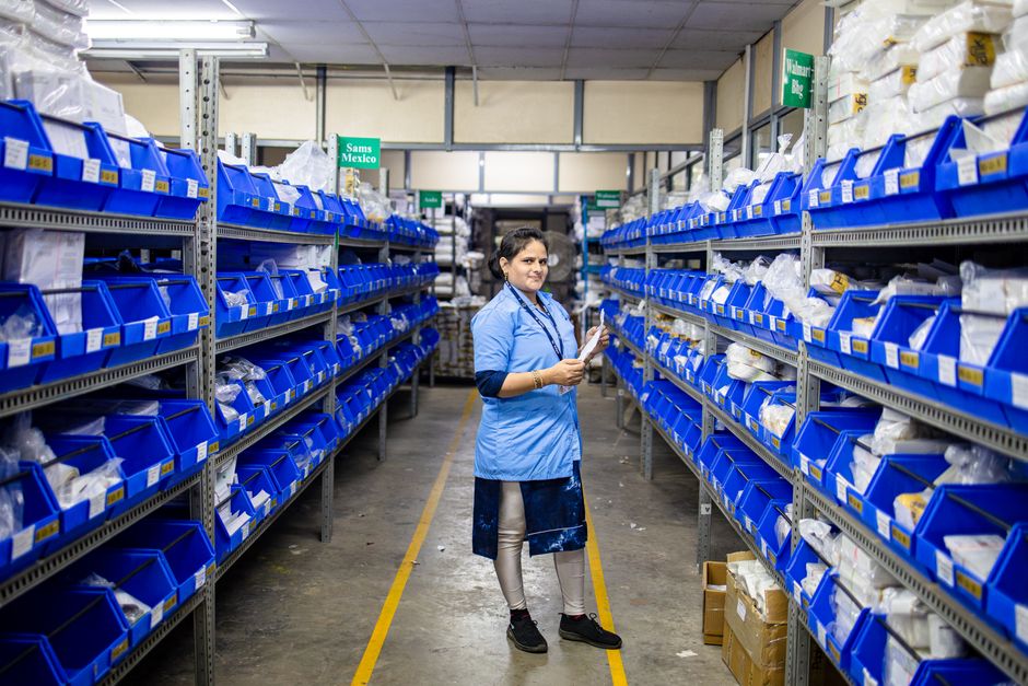 Female worker organizing inventory in a modern warehouse aisle, surrounded by blue storage bins.