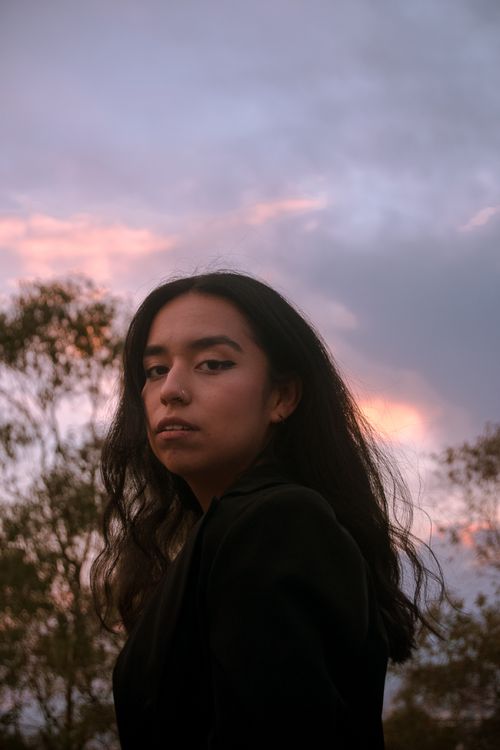 Free Portrait of a thoughtful woman outdoors at sunset with a colorful sky in the background. Stock Photo