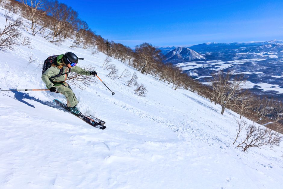 熟練したスキーヤーが、晴れた冬の日に雪山の斜面を滑り降り、ダイナミックな動きを披露します。