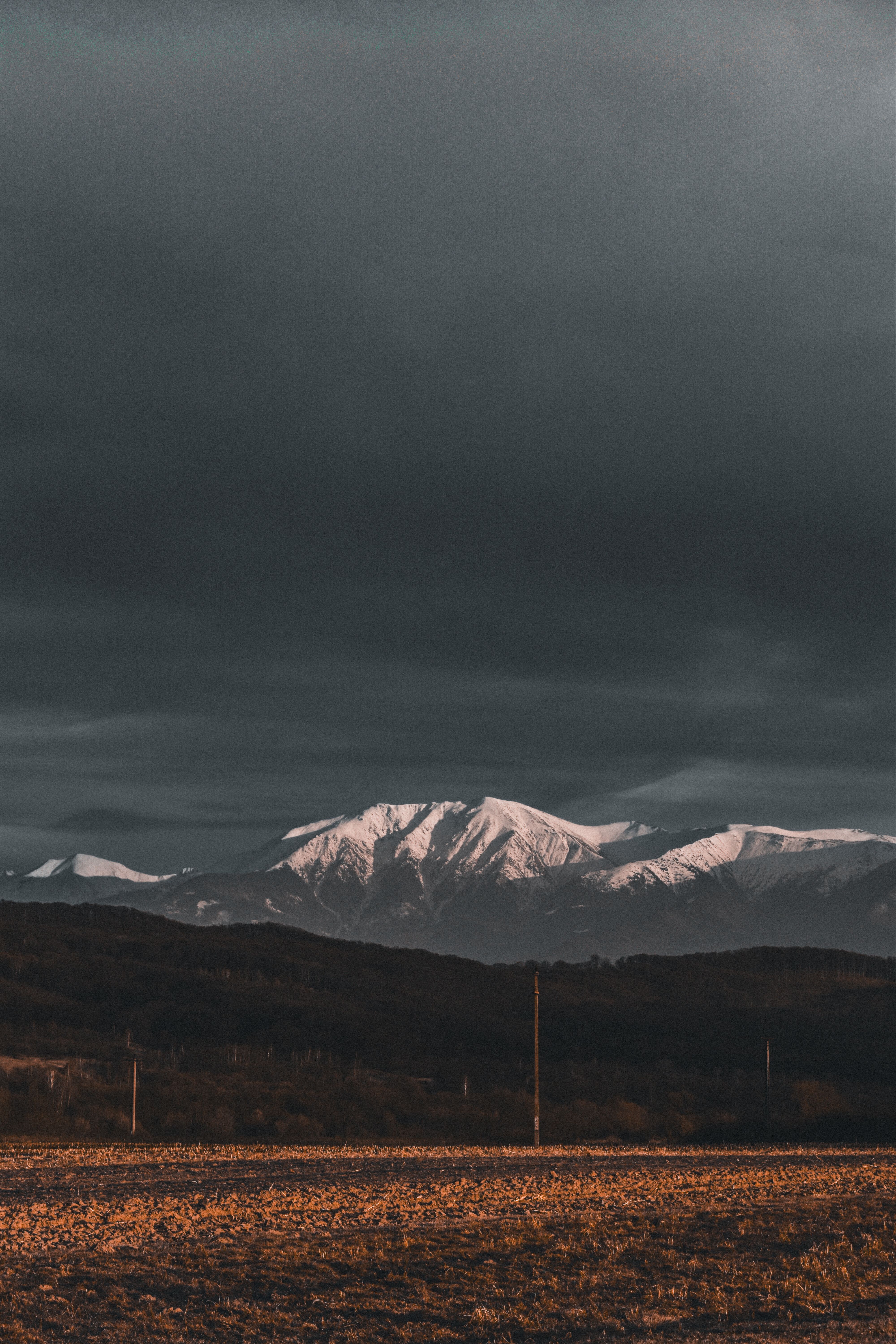 A breathtaking view of snow-capped mountains under a stormy sky at sunset.