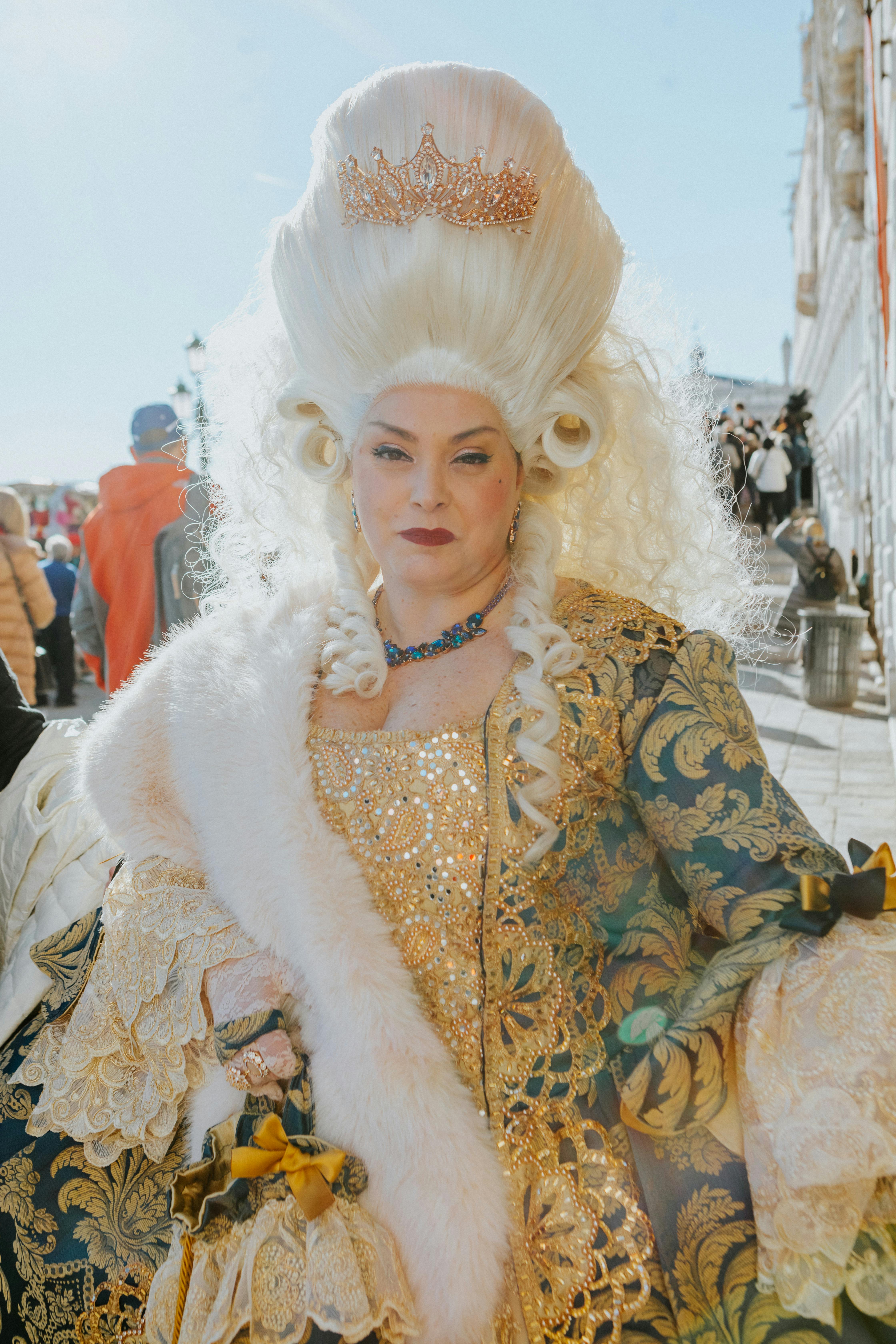 Regal woman in elaborate costume at Venice Carnival under bright daylight.