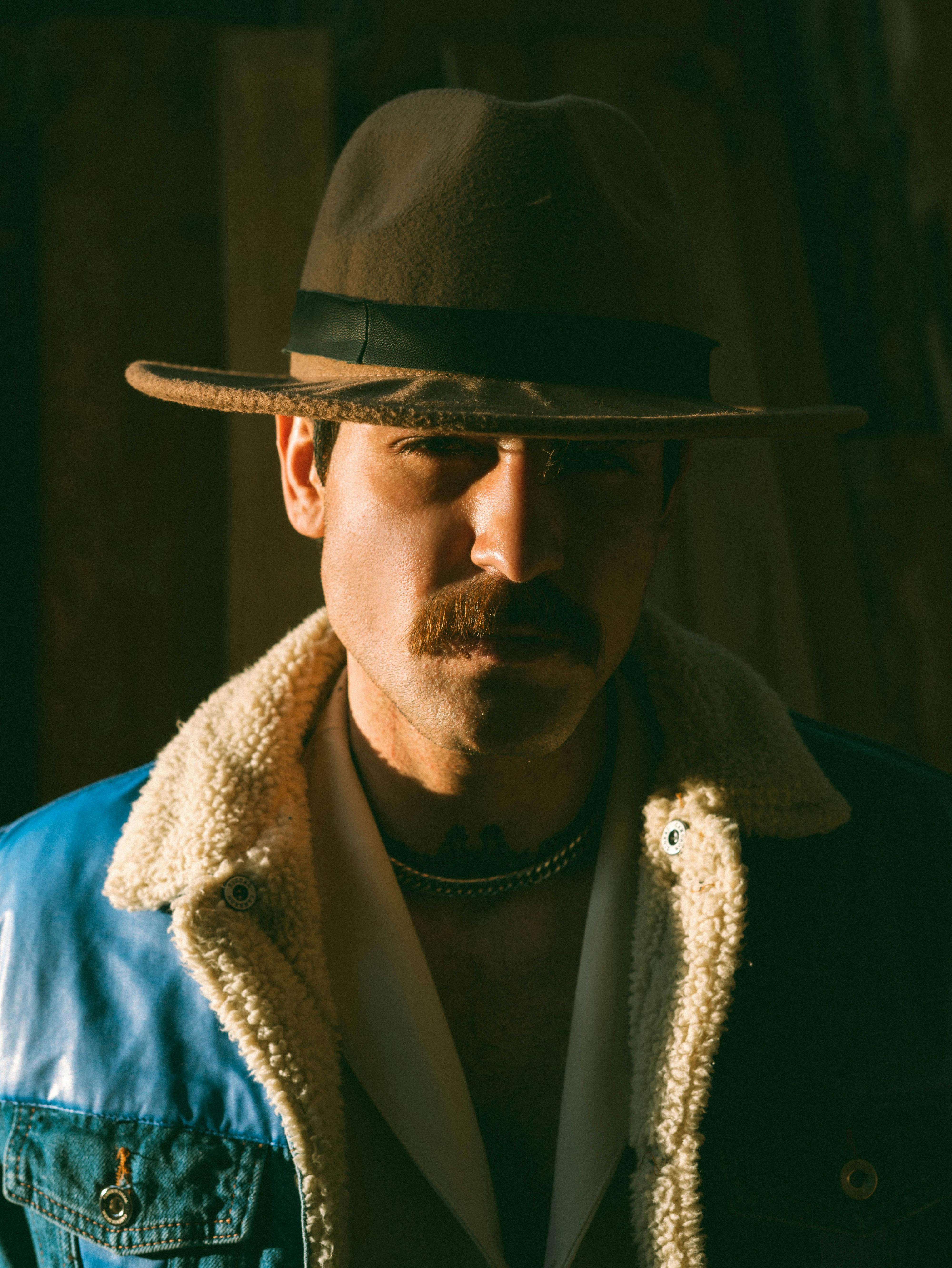 A dramatic portrait of a man in a fedora with a sunlit face, showcasing a moody atmosphere.