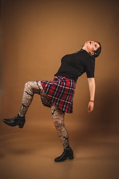Woman poses expressively in studio wearing plaid skirt and fishnet stockings for bold artistic style.