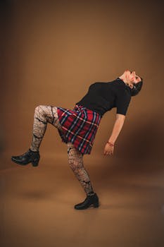 Fashion-forward woman in plaid skirt and fishnets strikes a unique pose in studio setting.