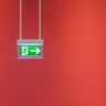 A bright green illuminated emergency exit sign hanging against a vibrant solid red wall.