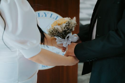 Close-up of a couple holding hands with a bouquet during a wedding ceremony, symbolizing love and commitment.