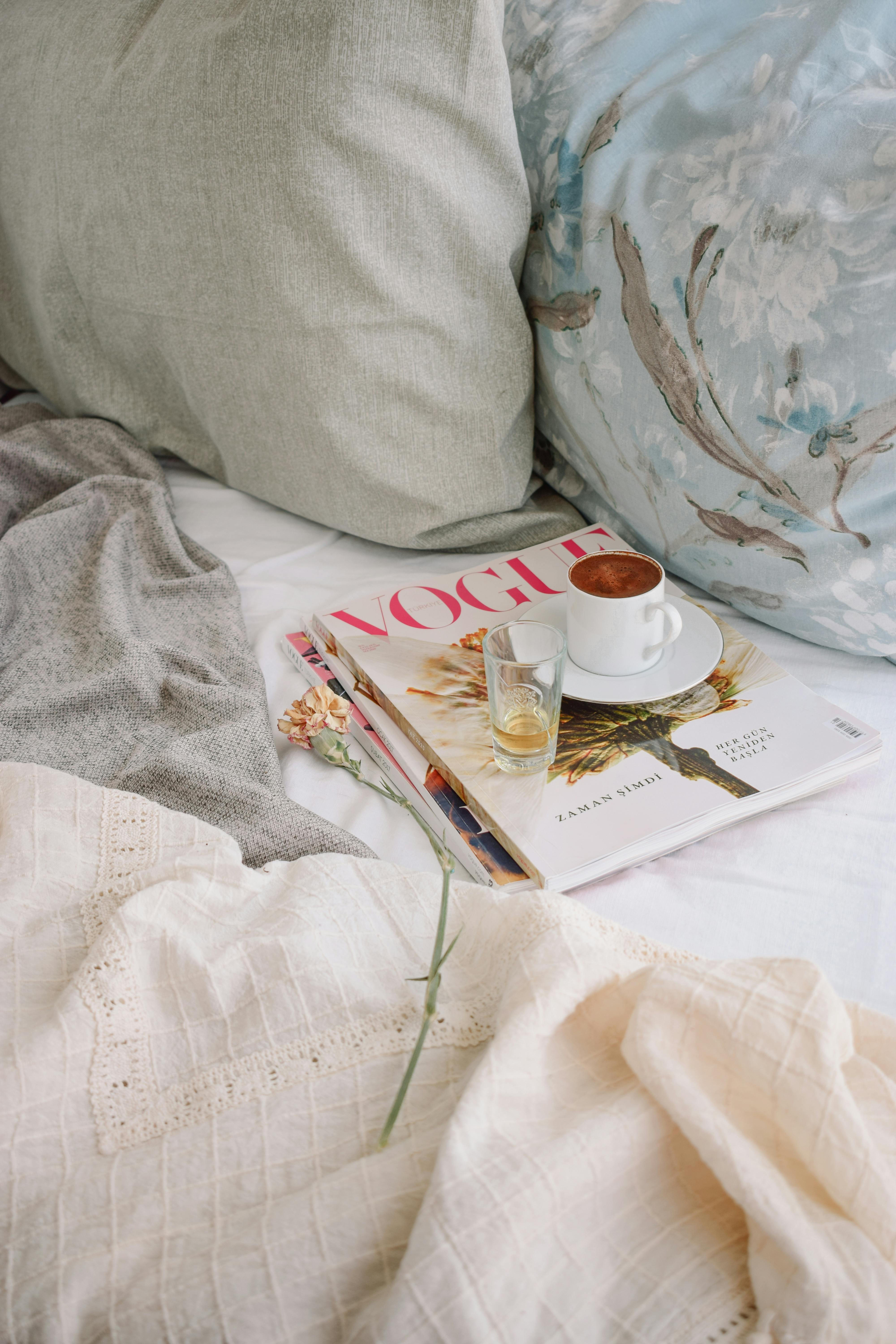 Relaxing morning with coffee and Vogue magazine on a comfortable bed.